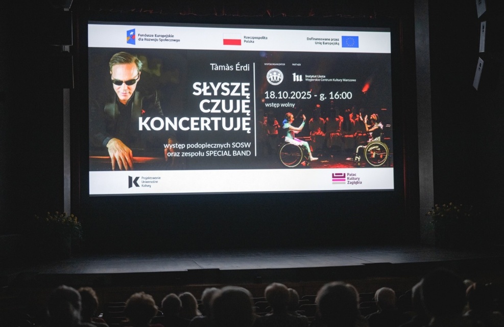 Zdjęcie z&nbsp;sali koncertowej w&nbsp;Pałacu Kultury Zagłębia. Publiczność jest zwrócona w&nbsp;stronę dużego ekranu, na&nbsp;którym wyświetlono grafikę informacyjną o&nbsp;koncercie. Grafika zawiera zdjęcie niewidomego pianisty Tamasa Edrila oraz nazwę wydarzenia - słyszę, czuję, koncertuję