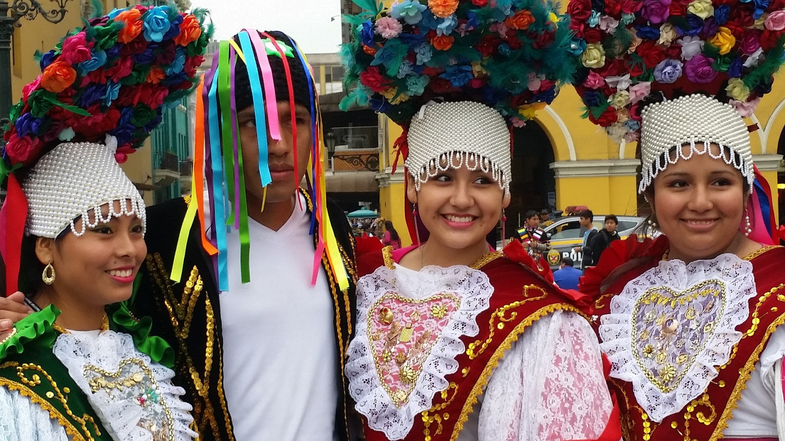 Na zdjęciu znajdują się cztery osoby - trzy kobiety i jeden mężczyzna. Na głowach mają kolorowe wianki. Ubrani są w kolorowe stroje ludowe - peruwiańskie. 