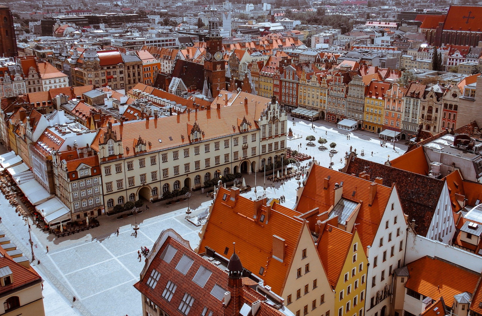 Na zdjęciu znajduje się panorama rynku, we Wrocławiu. Kamienice z czerwonymi dachami stoją wokół rynku. Kamienice i rynek widoczne są z lotu ptaka, z góry.