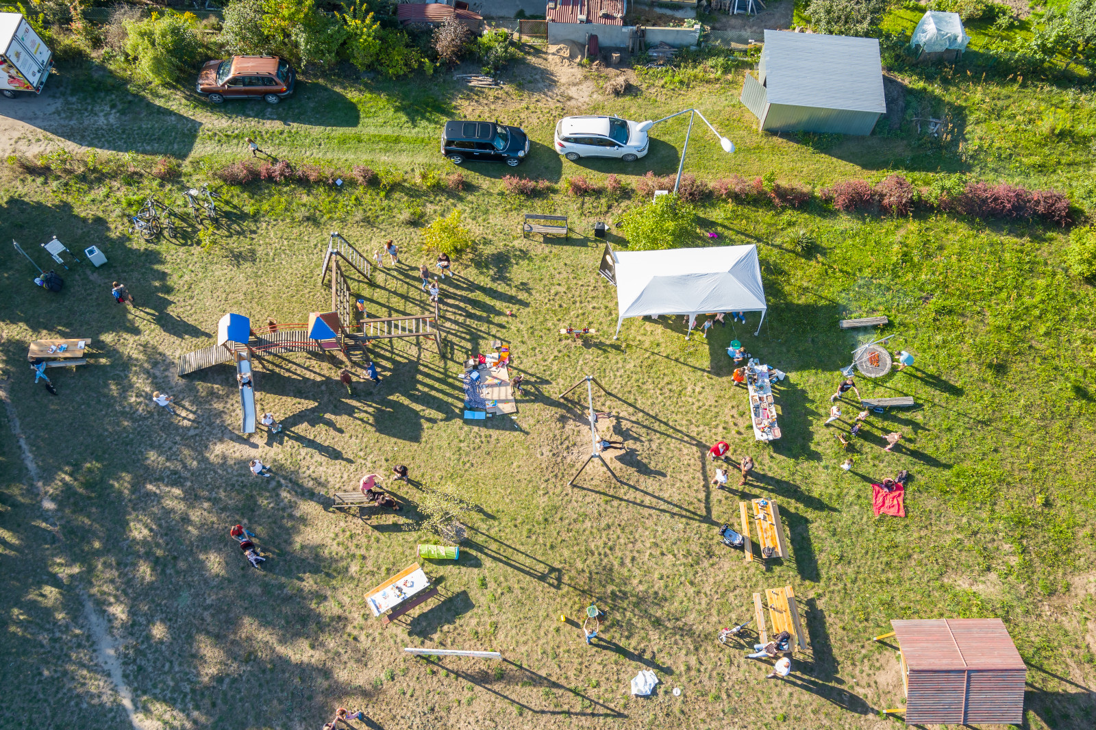 Zdjęcie z drona z wysokości widać ludzi biorących udział w pikniku jest rozłożone białe zadaszenie, stoją ławy i stoły.