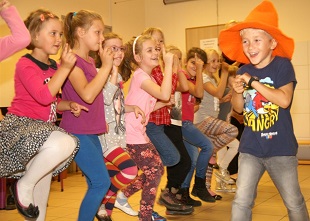 chłopiec w pomarańczowym kapeluszu i rządek tańczących dziewcząt